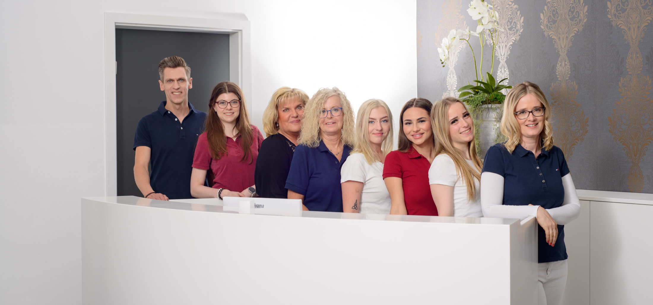 Das Team der Zahnarztpraxis in Steglitz hinter dem Empfang der Praxis